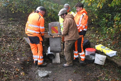 Arbeiter in orangefarbener Kleidung richten einen Grenzstein aus.