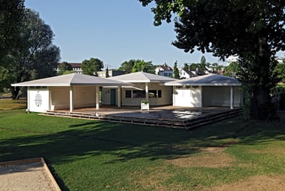 Moderner Pavillon im Grünen mit Bäumen im Hintergrund.",