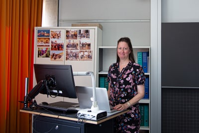 FMS-Lehrerin Kathrin Urscheler steht an einem Schreibtisch mit Computer in einem Klassenzimmer..