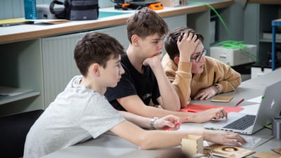 Drei Jungen konzentrieren sich auf einen Laptop im Klassenzimmer.",