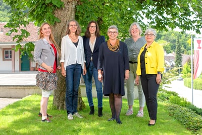 Sechs Frauen stehen vor einem Baum im Freien.