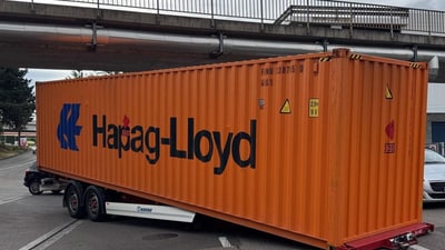 Grosser orangefarbener Container auf einem Anhänger unter einer Brücke festgefahren.