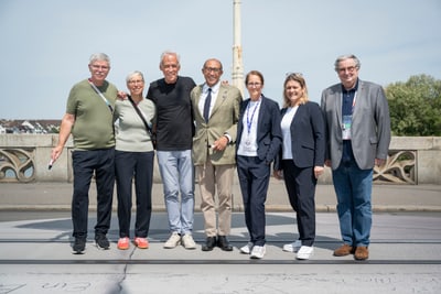 Gruppe von sieben Menschen steht auf einer Brücke bei sonnigem Wetter.