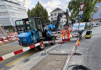 Strassenbaustelle mit Maschinen und Arbeitern in orangefarbener Kleidung.