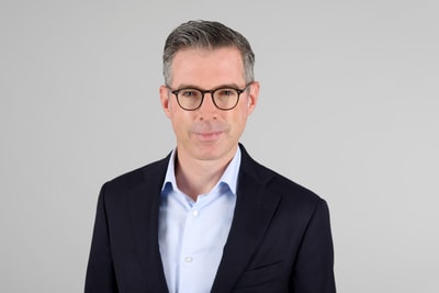 Der neue Leiter der Steuerverwaltung Basel-Stadt Thomas Beda Fischerim Anzug mit Brille vor grauem Hintergrund.