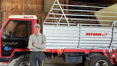 Ein Mann steht vor einem landwirtschaftlichen Fahrzeug in einem Holzgebäude.