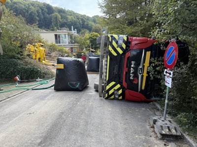 Umgekippter LKW auf Strasse mit Absperrungen und Natur im Hintergrund.