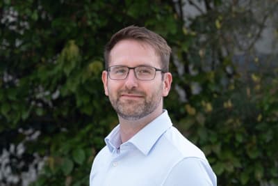 Person mit Brille und Hemd vor Pflanzenhintergrund.