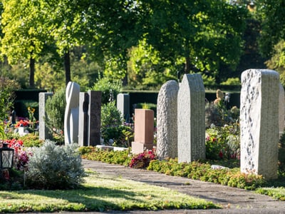 Reihe von Grabsteinen auf einem Friedhof bei Tageslicht.