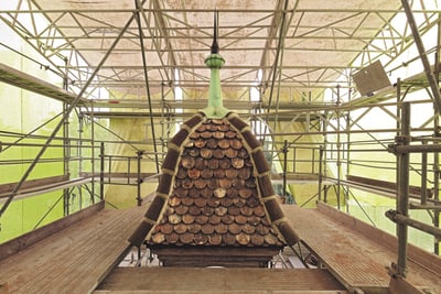 Gerüst umgibt kleines Dach mit Schindeln und Turmspitze.