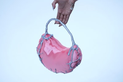 Hand hält rosafarbene Tasche mit silbernen Details.