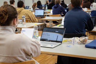 Studenten im Raum mit Laptops und Notizen bei einer Prüfung.