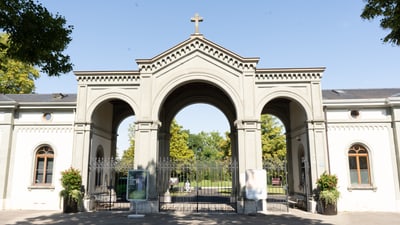 Historisches Tor mit Kreuz, umgeben von Bäumen.