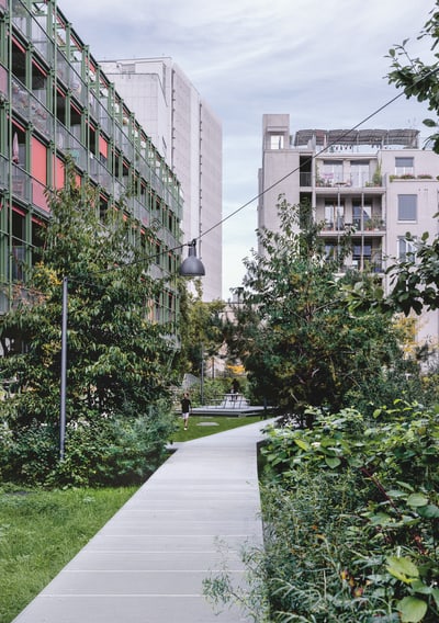 Gehweg zwischen modernen Gebäuden und grünen Bäumen.