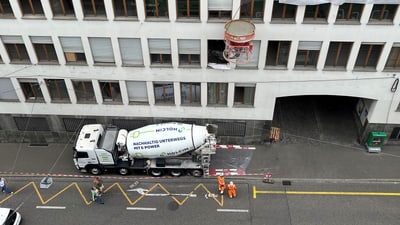 Betonmischer-Lkw auf Stadtstrasse neben Gebäude, mit Bauarbeitern.