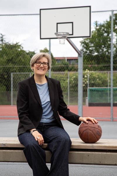 Sarah Thönen sitzt auf Bank mit Basketballkorb im Hintergrund.