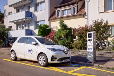 Elektroauto lädt an Ladestation vor Wohngebäude.