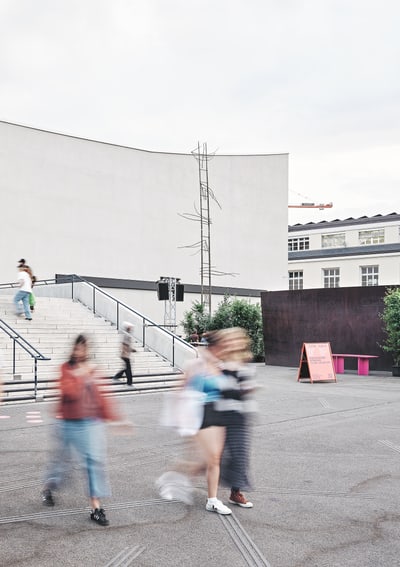 Menschen gehen draussen an einer weissen Wand vorbei.