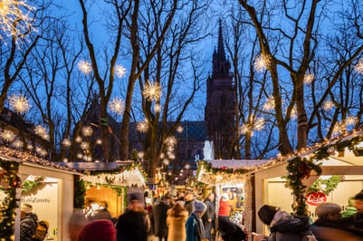Beleuchteter Weihnachtsmarkt bei Abenddämmerung mit Kirche im Hintergrund.