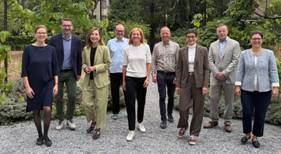 Gruppe von Personen, die auf einem Kiesweg stehen, von Bäumen umgeben.