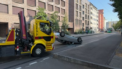 Abschleppwagen neben umgekipptem Auto in städtischer Strasse.