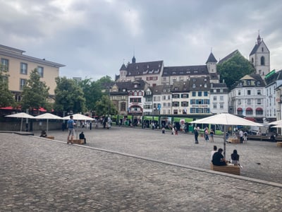 Menschen auf einem gepflasterten Platz mit historischen Gebäuden im Hintergrund.