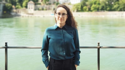 Frau mit Brille steht vor einem Flussgeländer.