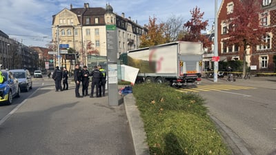 Strassenszene mit Polizeipräsenz neben einem Lastwagen und Wohnhäusern im Hintergrund.