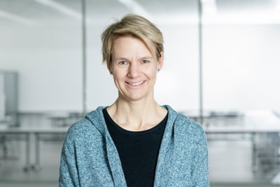 Nicole Schwery lächelt in einem modernen Raum mit Glastrennwänden.