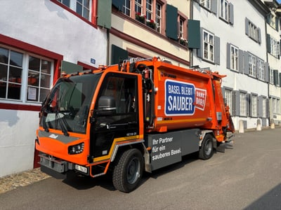 Orangefarbenes Müllfahrzeug in der Strasse geparkt.