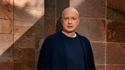 Sam Keller in dunkelblauer Kleidung vor einer Steinwand.