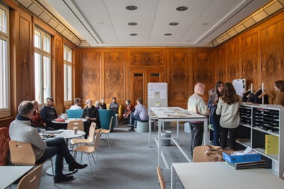 Personen in einem Raum mit Holzwänden arbeiten in Gruppen zusammen.