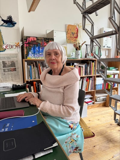 Eine Person sitzt an einem Schreibtisch mit Bücherregalen im Hintergrund.