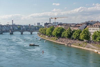 Rhein in Basel mit Brücke und Stadtansicht, Boote sichtbar.