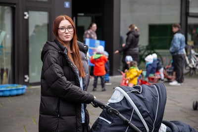 Charlotte André mit Kinderwagen vor Gebäude, Kinder im Hintergrund.