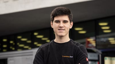 Mann vor Gebäude mit grossen Fenstern, trägt schwarzen Pullover.