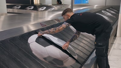Mann prüft Förderband mit Fussballmotiv am Flughafen.