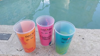 Drei bunte Eurovision-Becher am Beckenrand.