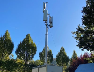 Hoher Mobilfunkmast von Bäumen umgeben.