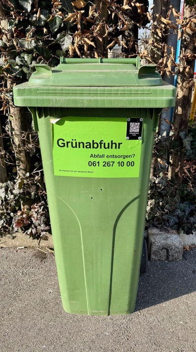 Grüner Müllcontainer mit Aufschrift 'Grünabfuhr'.