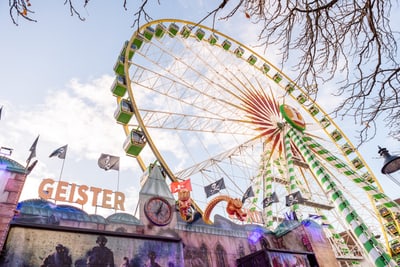Riesenrad und Geisterbahn auf Jahrmarkt mit Baumzweigen im Vordergrund.