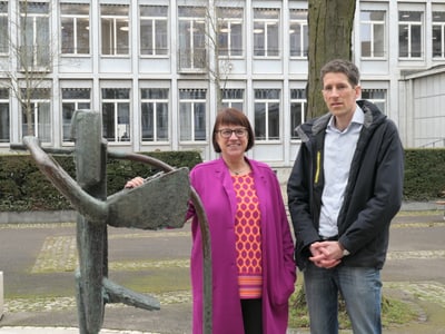 Zwei Personen stehen neben einer Skulptur vor einem Gebäude.