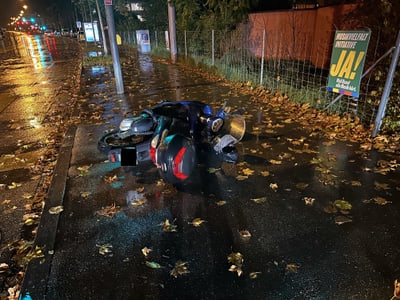 Umgestürztes Motorrad auf nasser Strasse bei Nacht mit Herbstlaub.",