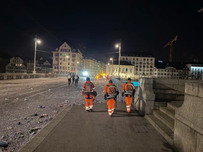Drei Arbeiter in orangefarbenen Anzügen auf einer Brücke bei Nacht.