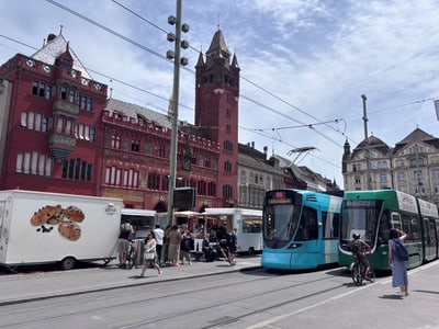 Eine belebte Strassenszene mit bunten Gebäuden, Strassenbahn und Menschen.