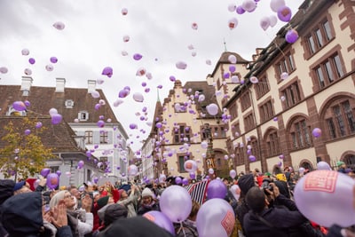 Menschenmenge mit lila Luftballons in historischer Stadtumgebung.