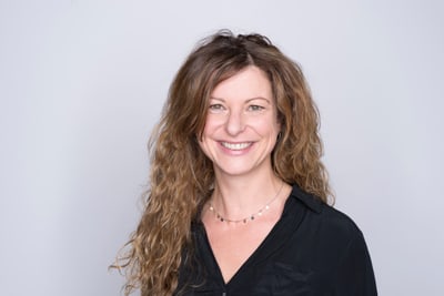 Frau mit lockigem Haar und schwarzem Hemd lächelt.