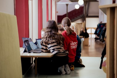 Kinder sitzen auf dem Boden mit Laptops in einem Schulflur.