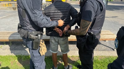 Person wird von zwei Polizisten in Handschellen gelegt.