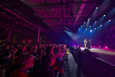 Menschenmenge bei einer Bühnenshow in lila Licht.